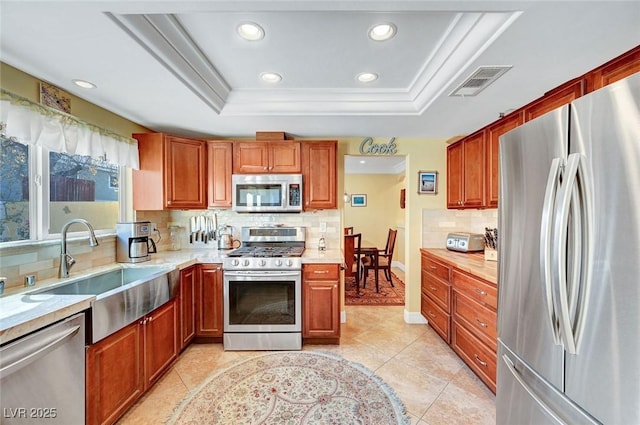 kitchen with light tile patterned flooring, a raised ceiling, tasteful backsplash, sink, and stainless steel appliances