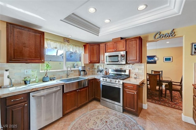 kitchen featuring appliances with stainless steel finishes, sink, hanging light fixtures, light tile patterned floors, and a tray ceiling