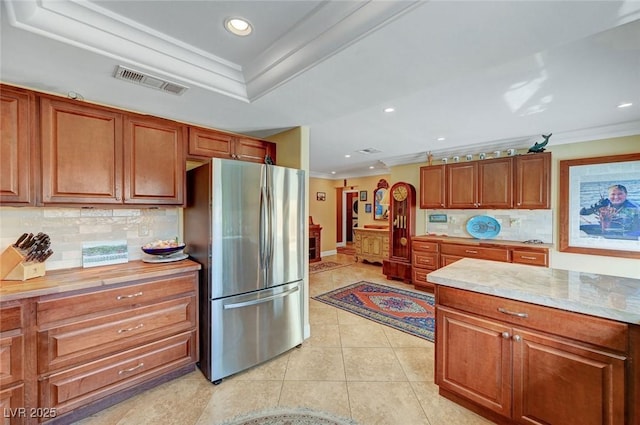 kitchen featuring light tile patterned flooring, crown molding, stainless steel fridge, a raised ceiling, and decorative backsplash