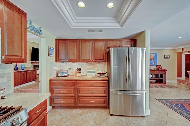 kitchen with appliances with stainless steel finishes, decorative backsplash, ornamental molding, light tile patterned floors, and a raised ceiling