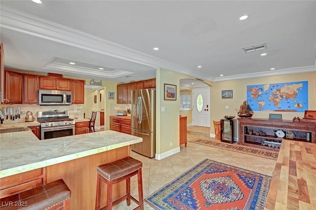 kitchen featuring crown molding, a breakfast bar area, appliances with stainless steel finishes, a raised ceiling, and kitchen peninsula