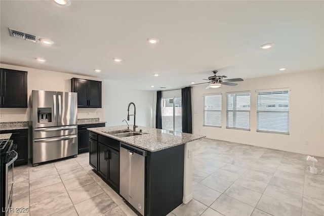 kitchen featuring sink, light stone counters, ceiling fan, stainless steel appliances, and a kitchen island with sink