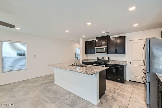 kitchen featuring sink, a kitchen island with sink, stainless steel appliances, a wealth of natural light, and light stone countertops