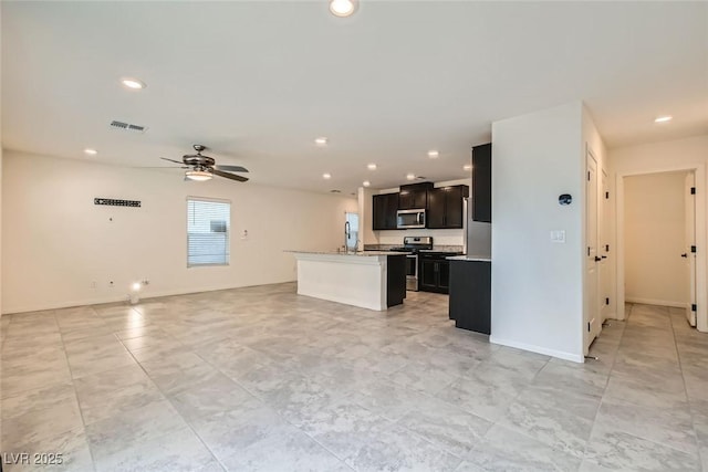 kitchen featuring appliances with stainless steel finishes, a center island with sink, light stone counters, and ceiling fan