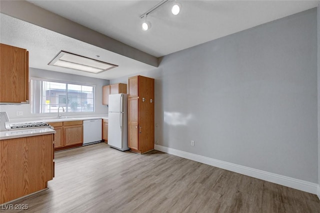 kitchen with rail lighting, sink, white appliances, and light wood-type flooring