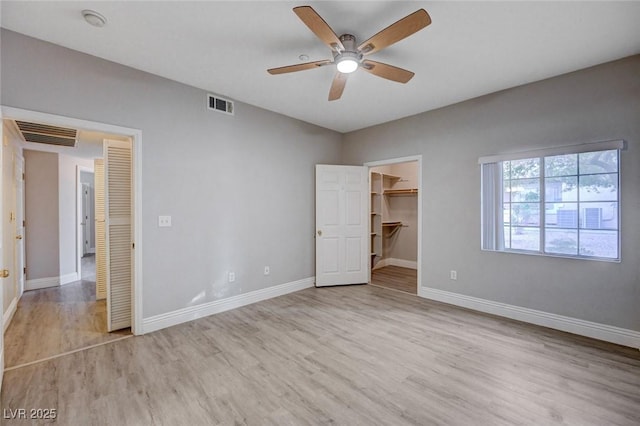 unfurnished bedroom with a closet, a spacious closet, ceiling fan, and light hardwood / wood-style flooring