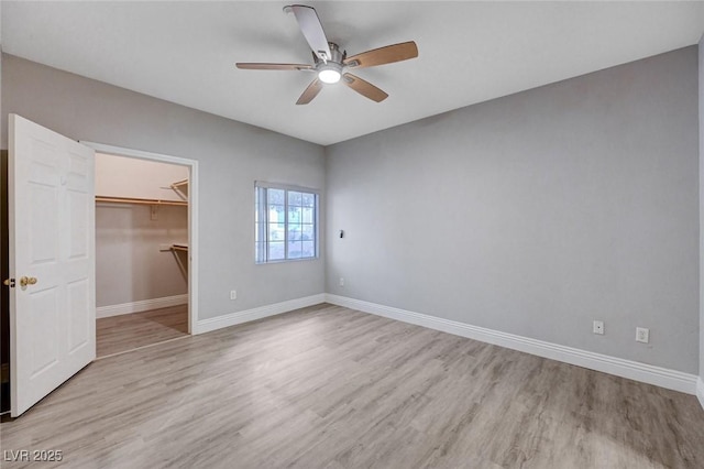 unfurnished bedroom featuring a walk in closet, light hardwood / wood-style flooring, a closet, and ceiling fan