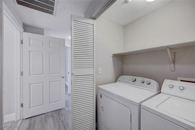 clothes washing area featuring washing machine and clothes dryer and light wood-type flooring