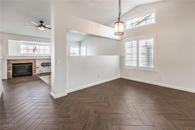 unfurnished dining area with ceiling fan, dark parquet flooring, a fireplace, and vaulted ceiling