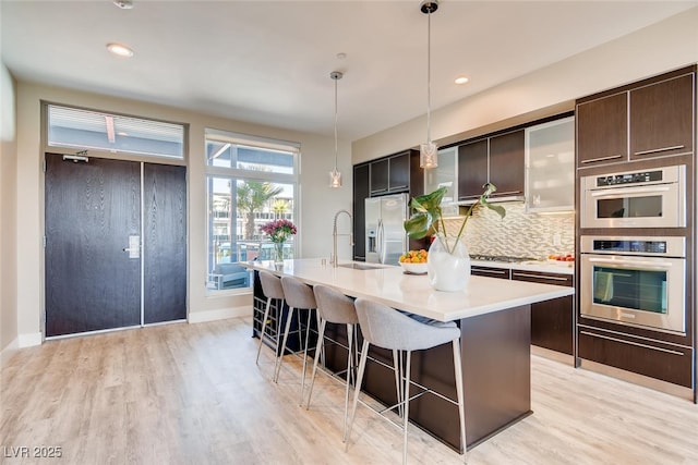 kitchen with appliances with stainless steel finishes, a kitchen island with sink, pendant lighting, and backsplash