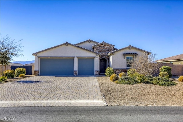 view of front of house featuring stucco siding, decorative driveway, stone siding, fence, and a garage