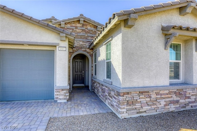 entrance to property featuring stone siding, stucco siding, an attached garage, and a tile roof