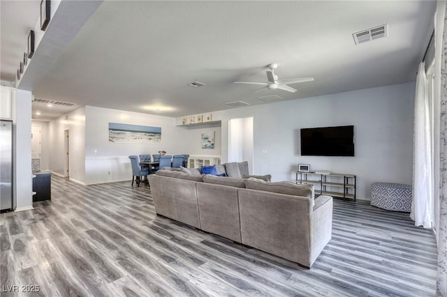 living room featuring ceiling fan, visible vents, and wood finished floors