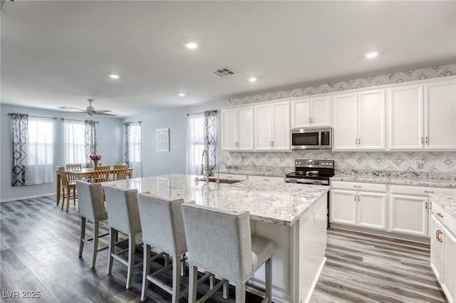 kitchen featuring visible vents, an island with sink, a sink, a kitchen breakfast bar, and appliances with stainless steel finishes