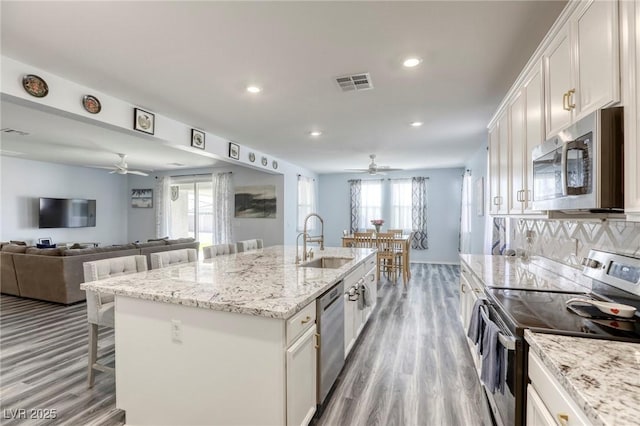 kitchen featuring a breakfast bar, a kitchen island with sink, a sink, stainless steel appliances, and white cabinetry