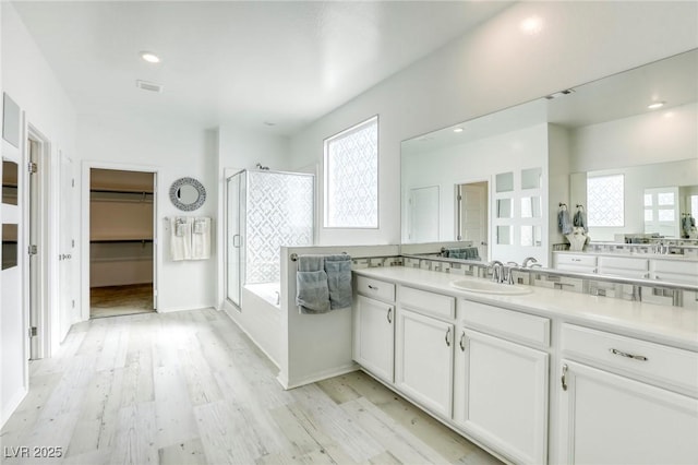 full bathroom featuring a walk in closet, a stall shower, wood finished floors, a bath, and vanity