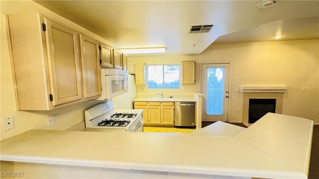 kitchen featuring light brown cabinetry, sink, kitchen peninsula, white appliances, and a tiled fireplace