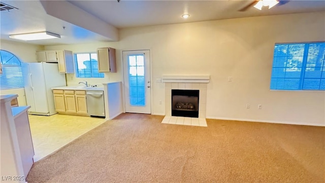 unfurnished living room with a tiled fireplace, sink, and light colored carpet