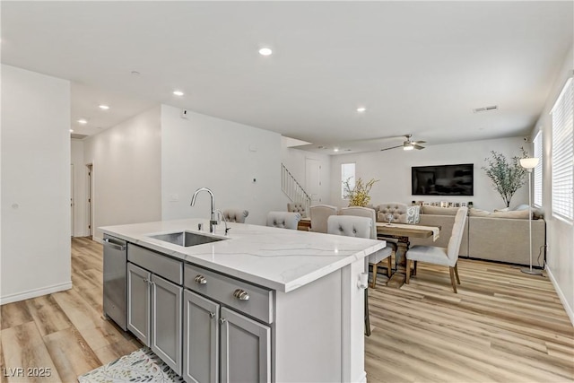 kitchen with sink, light hardwood / wood-style flooring, stainless steel dishwasher, gray cabinets, and an island with sink