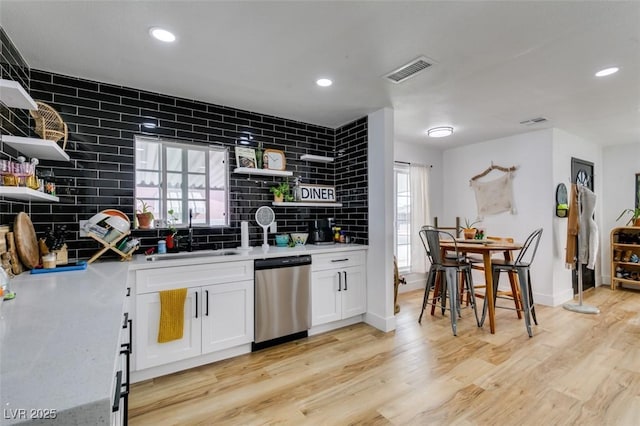 kitchen with sink, light wood-type flooring, dishwasher, decorative backsplash, and white cabinets