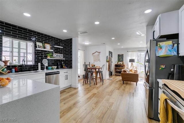 kitchen featuring sink, white cabinetry, light wood-type flooring, appliances with stainless steel finishes, and decorative backsplash