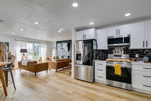 kitchen featuring tasteful backsplash, stainless steel appliances, white cabinets, and light wood-type flooring