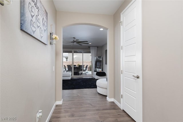 corridor featuring arched walkways, wood finished floors, and baseboards