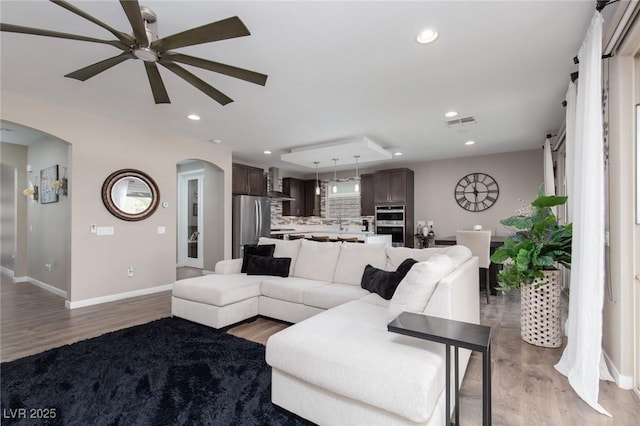 living room with light wood-style floors, arched walkways, visible vents, and recessed lighting