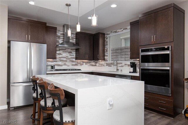 kitchen with appliances with stainless steel finishes, a breakfast bar, decorative backsplash, a center island, and wall chimney range hood