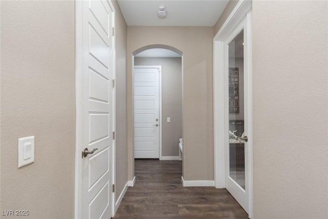 corridor featuring dark wood-style floors, arched walkways, and baseboards