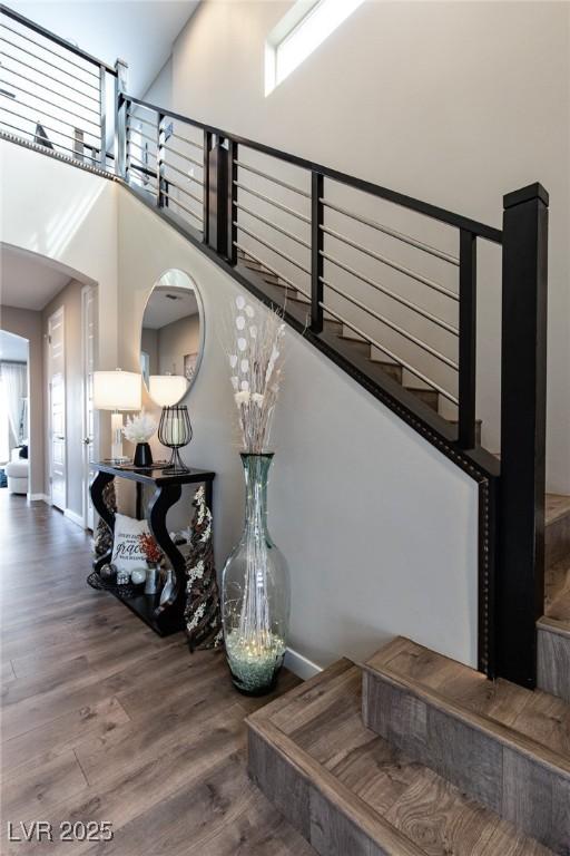 staircase featuring wood finished floors, a towering ceiling, and baseboards