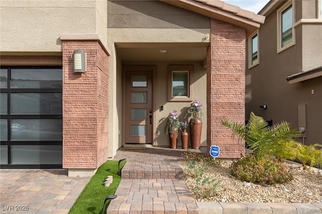 entrance to property featuring a garage, stucco siding, and brick siding