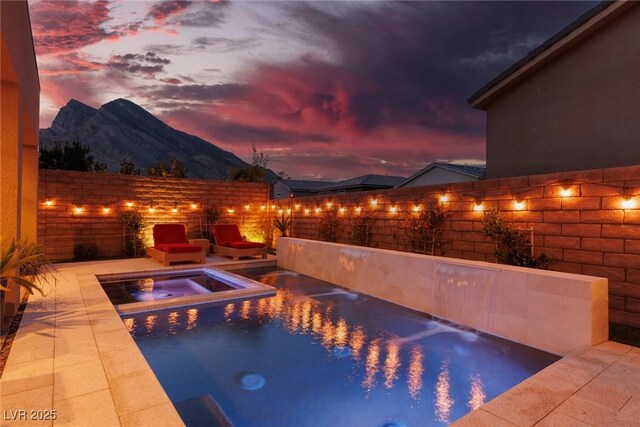 pool at dusk featuring a mountain view, a patio, and an in ground hot tub