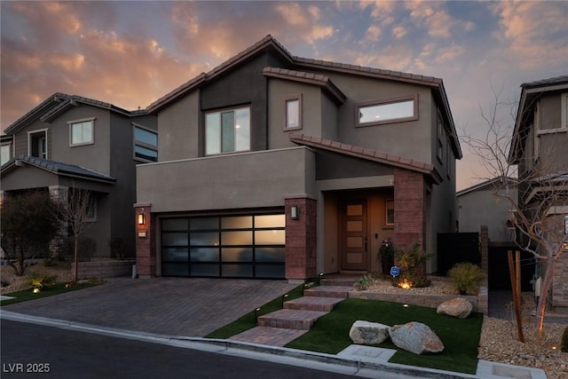 contemporary home featuring decorative driveway, a tile roof, brick siding, stucco siding, and a garage