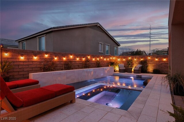 pool at dusk with an in ground hot tub and a patio area