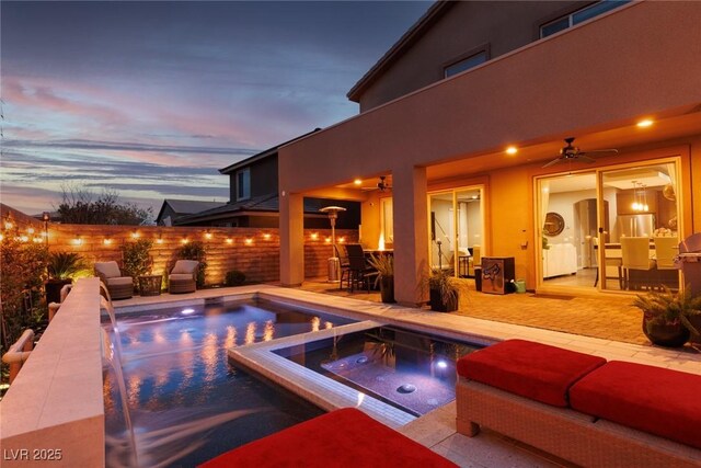 pool at dusk featuring an in ground hot tub, ceiling fan, a patio, and pool water feature