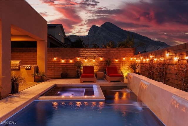 view of swimming pool with exterior kitchen, a mountain view, fence, and an in ground hot tub