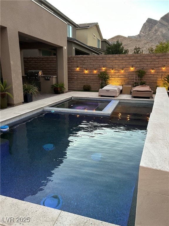 view of swimming pool featuring an outdoor kitchen, grilling area, an in ground hot tub, fence, and a mountain view