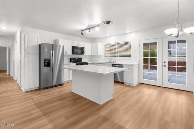 kitchen featuring sink, white cabinetry, hanging light fixtures, a kitchen island, and black appliances