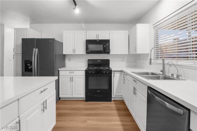 kitchen with sink, white cabinetry, light hardwood / wood-style flooring, track lighting, and black appliances