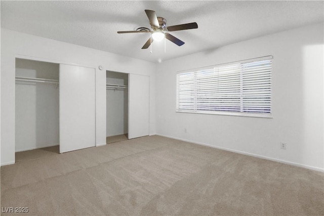 unfurnished bedroom with light carpet, ceiling fan, two closets, and a textured ceiling