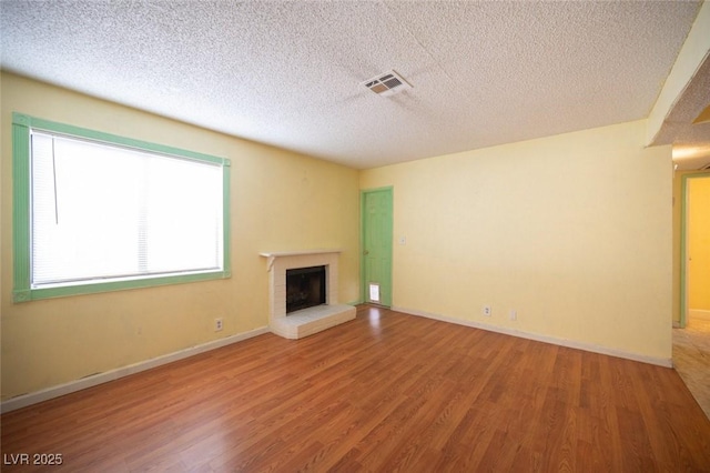 unfurnished living room featuring hardwood / wood-style flooring, a brick fireplace, and a textured ceiling