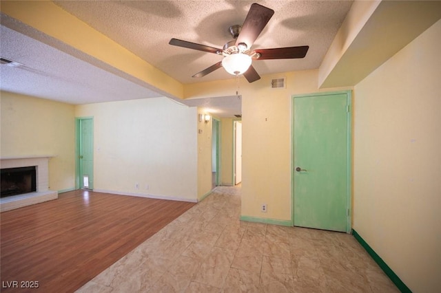unfurnished living room with a brick fireplace, light hardwood / wood-style flooring, a textured ceiling, and ceiling fan