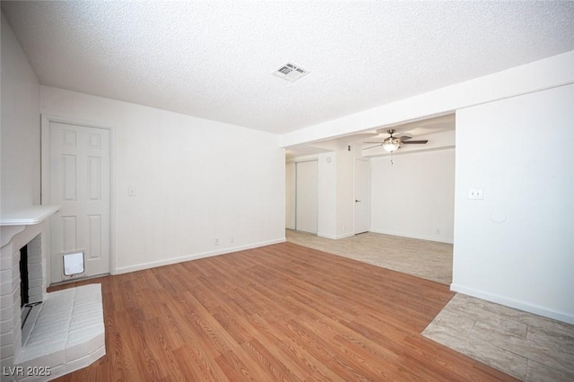 1701 E Katie Ave Unit 65, Las Vegas, NV 89119 - unfurnished living room with light wood-style flooring, a brick fireplace, a textured ceiling, ceiling fan, and baseboards