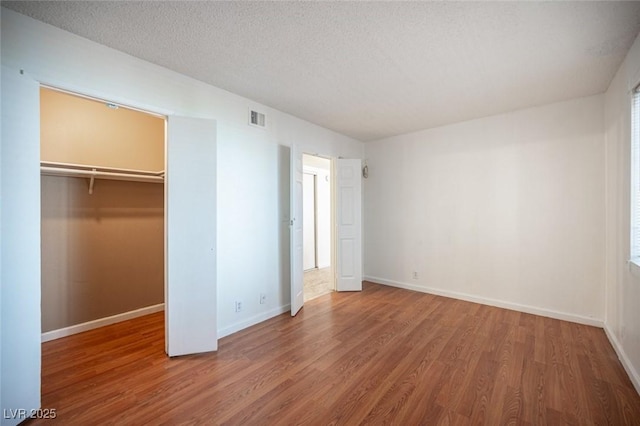 1701 E Katie Ave Unit 65, Las Vegas, NV 89119 - unfurnished bedroom with wood finished floors, a walk in closet, baseboards, and a textured ceiling