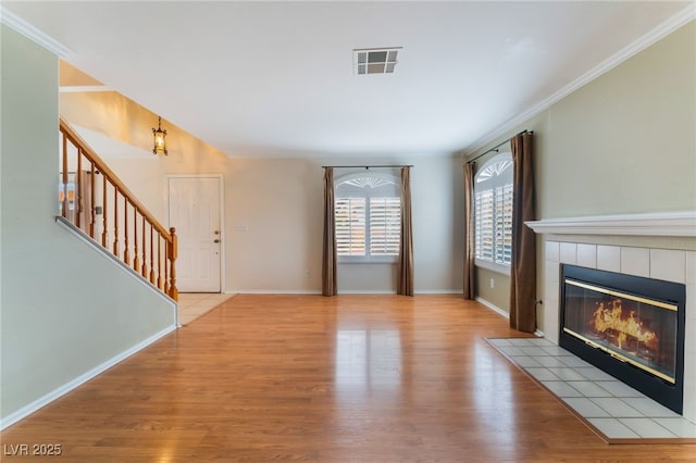 unfurnished living room featuring a tiled fireplace, ornamental molding, and light hardwood / wood-style floors