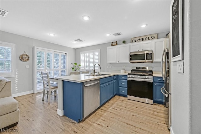 kitchen with blue cabinetry, stainless steel appliances, kitchen peninsula, and sink