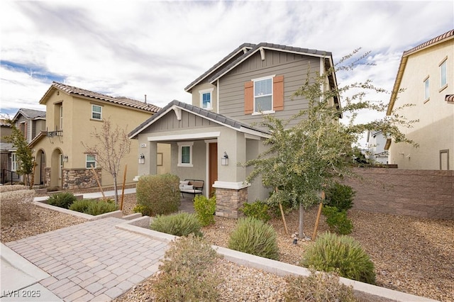 view of front of house with board and batten siding, stone siding, fence, and stucco siding