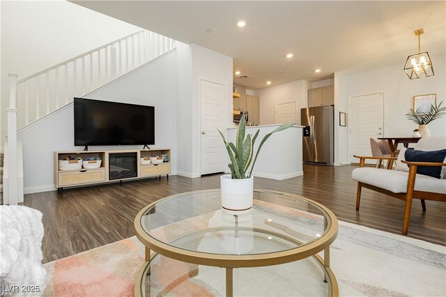 living area with recessed lighting, stairway, an inviting chandelier, dark wood-type flooring, and baseboards