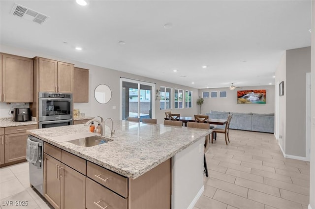 kitchen with a kitchen bar, sink, a center island with sink, stainless steel appliances, and light stone countertops